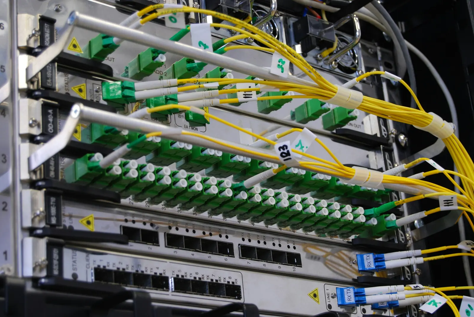 Yellow fibre patch cords on green SC adapters in an optical distribution frame above a switch